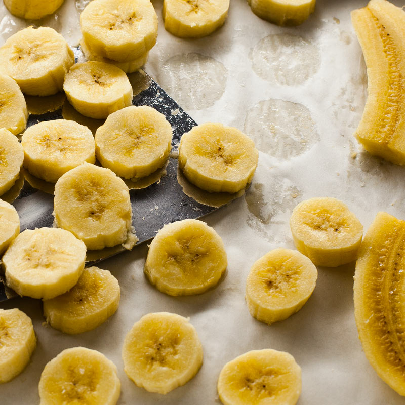 Plátanos congelados en rodajas y cuartos colocados en una placa con papel de horno