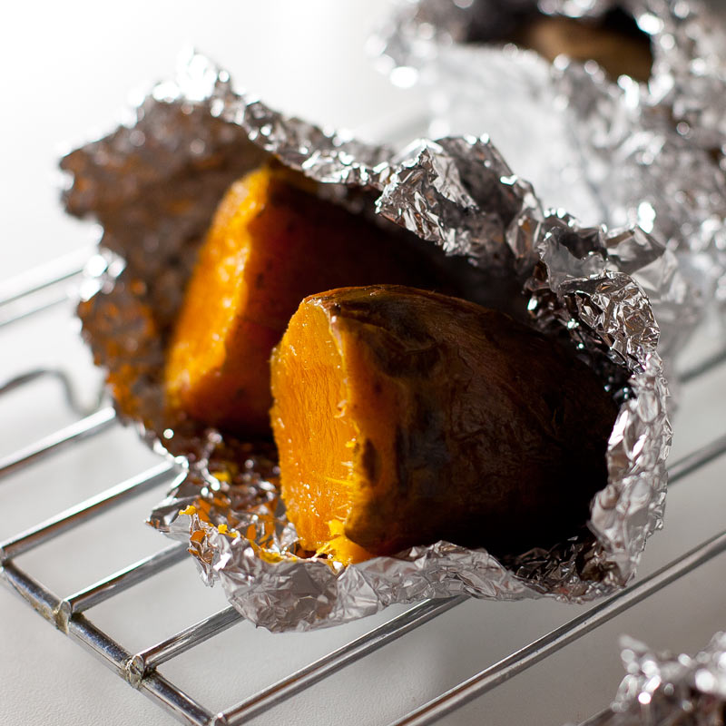 Boniato cortado a la mitad envuelto en papel aluminio, sobre bandeja de horno