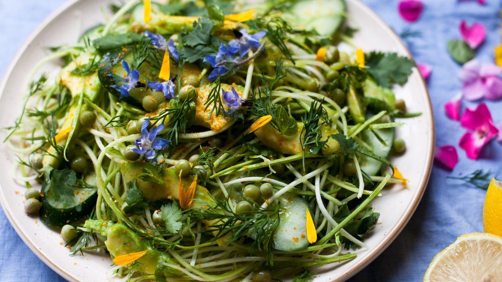 plato de fideos de calabacín con aguacate, pepino, cilantro, flores lobelias, guisantes y pétalos de caléndula