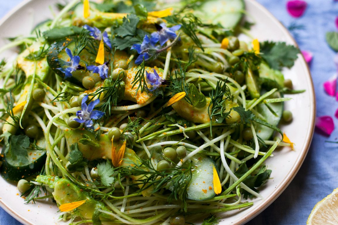 plato de fideos de calabacín con aguacate, pepino, cilantro, flores lobelias, guisantes y pétalos de caléndula