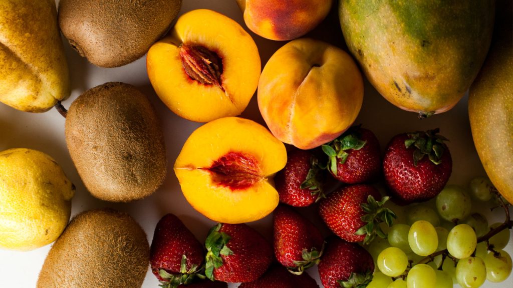 Melocotones, fresas, kiwis, mangos, limones, peras y kiwis sobre mesa blanca