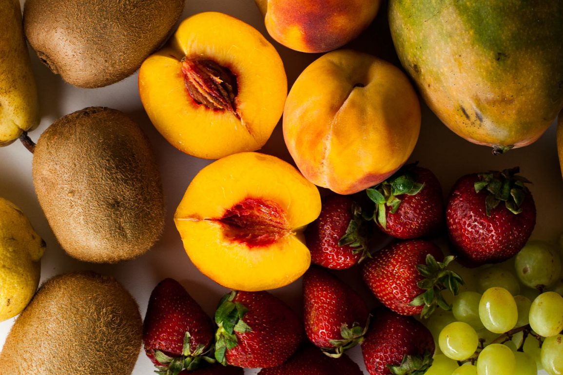 Melocotones, fresas, kiwis, mangos, limones, peras y kiwis sobre mesa blanca