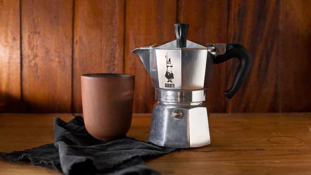 Cafetera moka Bialetti con taza de cerámica sobre mesa de madera