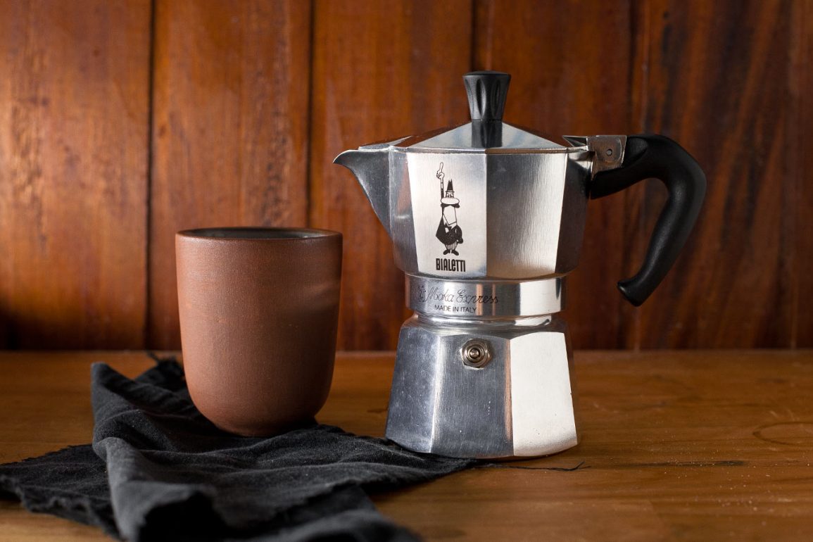 Cafetera moka Bialetti con taza de cerámica sobre mesa de madera