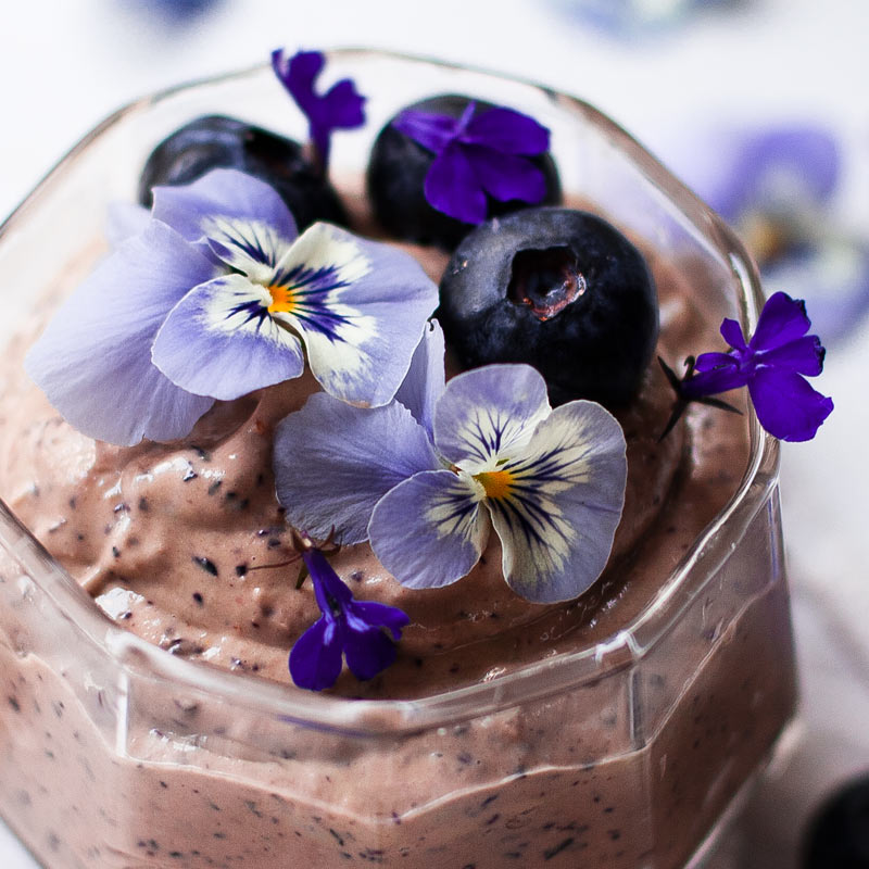 Mousse de arándanos y anarcados servido en vaso de vidrio con flores comestibles
