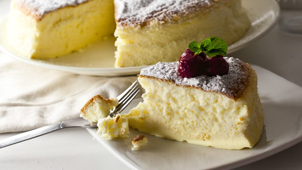 Porción de tarta cheesecake japonés decorada con frambuesas y hojas de menta, cortada con tenedor
