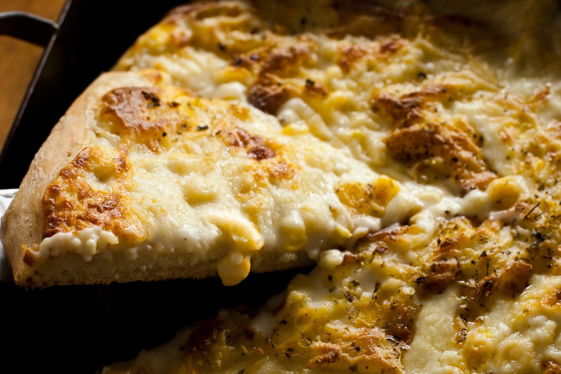 Porción de pizza de choclo y salsa blanca siendo sacada