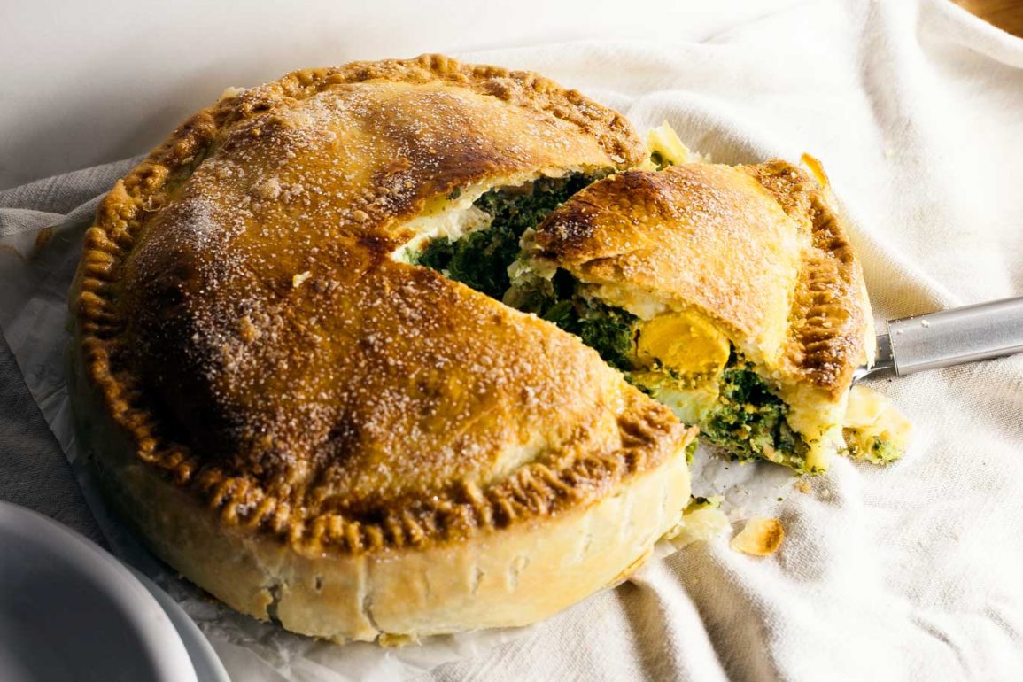 Tarta pasqualina con relleno de espinaca y huevo abierta sobre mantel de tela