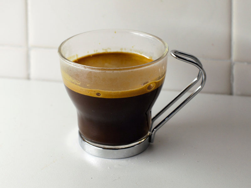 Café espresso en taza de vidrio y asa de metal sobre una mesa